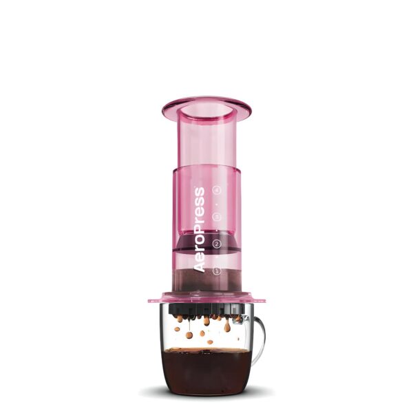Pink AeroPress coffee maker brewing fresh coffee in a glass mug.