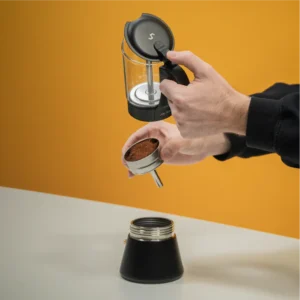 Person preparing the ClearBrew black Moka pot by Joy Resolve with coffee grounds in filter basket