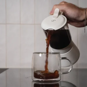 Pouring coffee from the ClearBrew white Moka pot by Joy Resolve into a glass cup