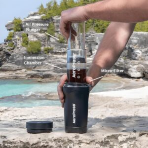 Aeropress Go Plus Travel System in black being used to brew coffee by the beach.