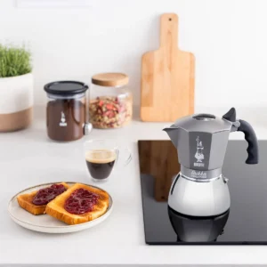 Bialetti Brikka Induction Moka Pot on an induction stovetop with breakfast and coffee cup